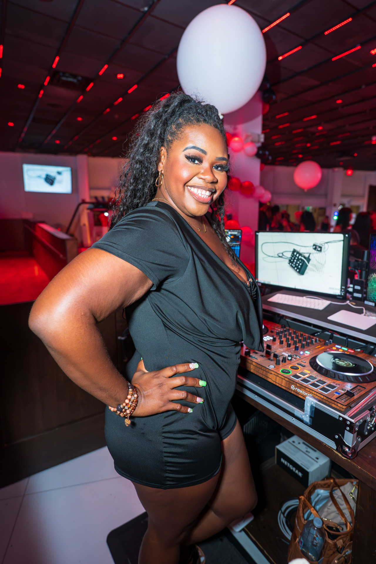 DJ Sam I Am beside her rekordbox setup under red club lighting
